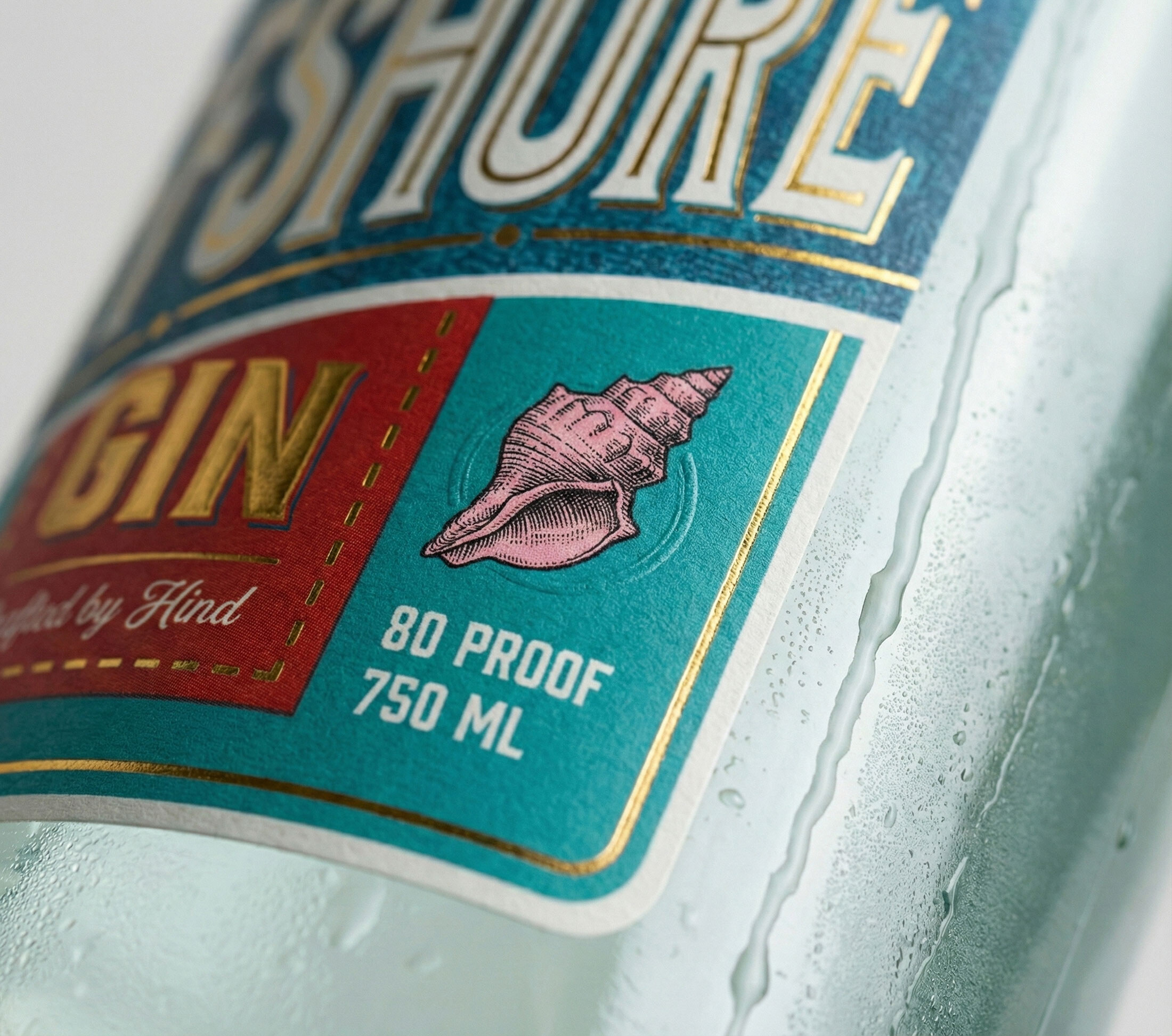 Macro of the label showing the engraved pink conch, gold foil and embossed detail on textured stock