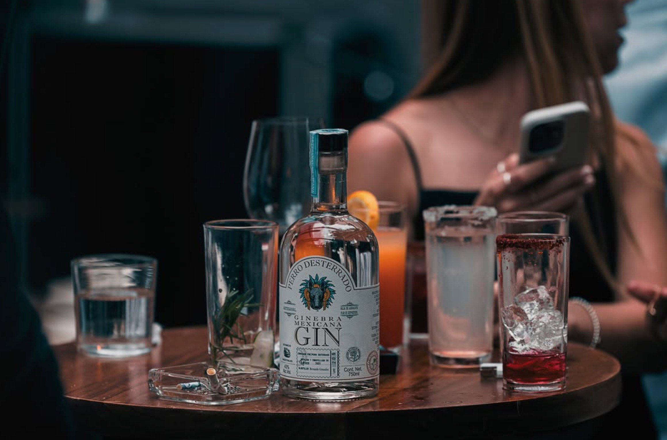 On a crowded bar table, glasses and an ashtray around it