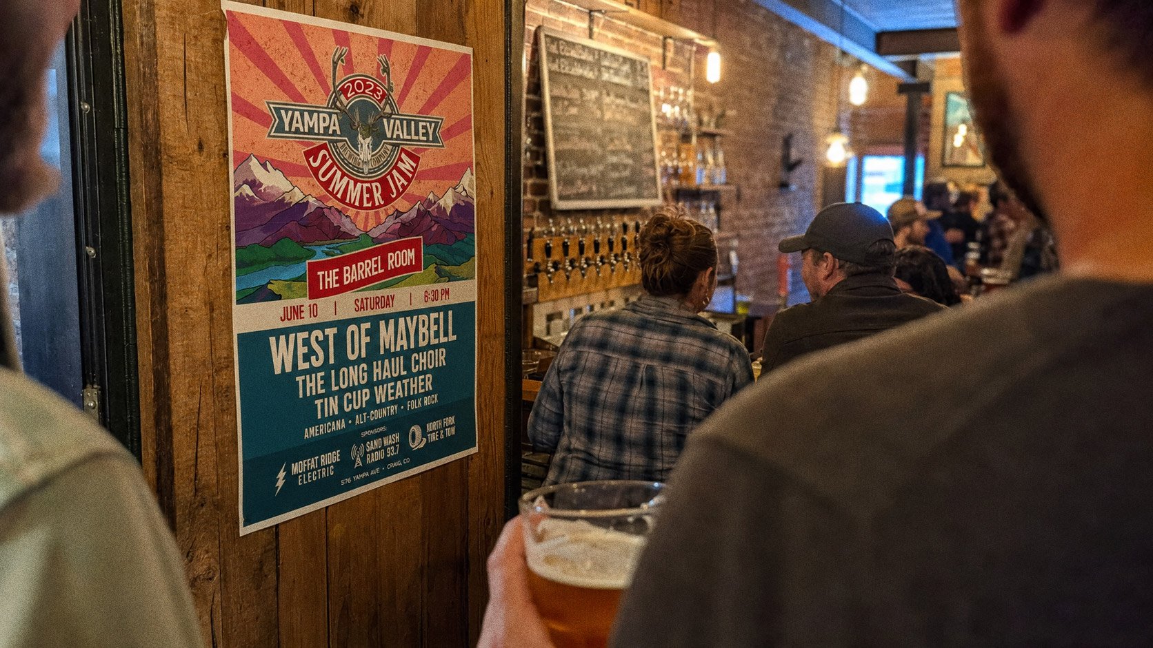 A stack of Summer Jam posters on the bar, masking tape, scissors and a beer beside them — mid print-run